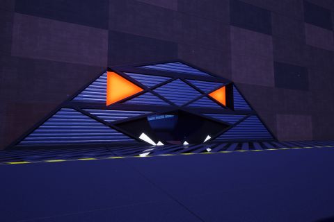 Image from the game Satisfactory featuring the entrance of a building made in the style of a grassy Minecraft-style dirt block. The entrance itself is the toothed maw or a glowing-eyed creature of some kind.